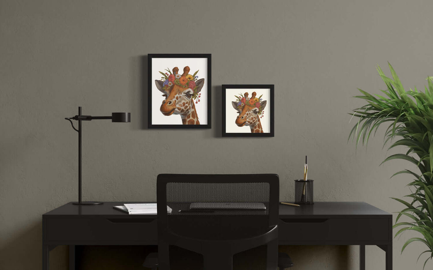 Blumenkind Giraffe prints displayed in black frames on a modern desk with green plant decor.