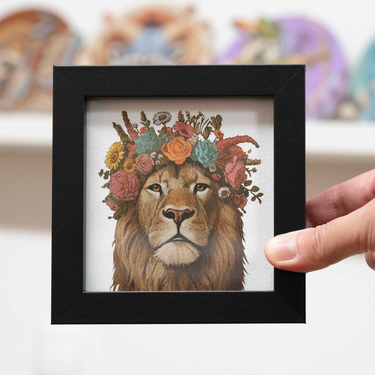 Pocket Art fine art print of a lion with a floral crown in a sleek black frame, 10 x 10 cm.