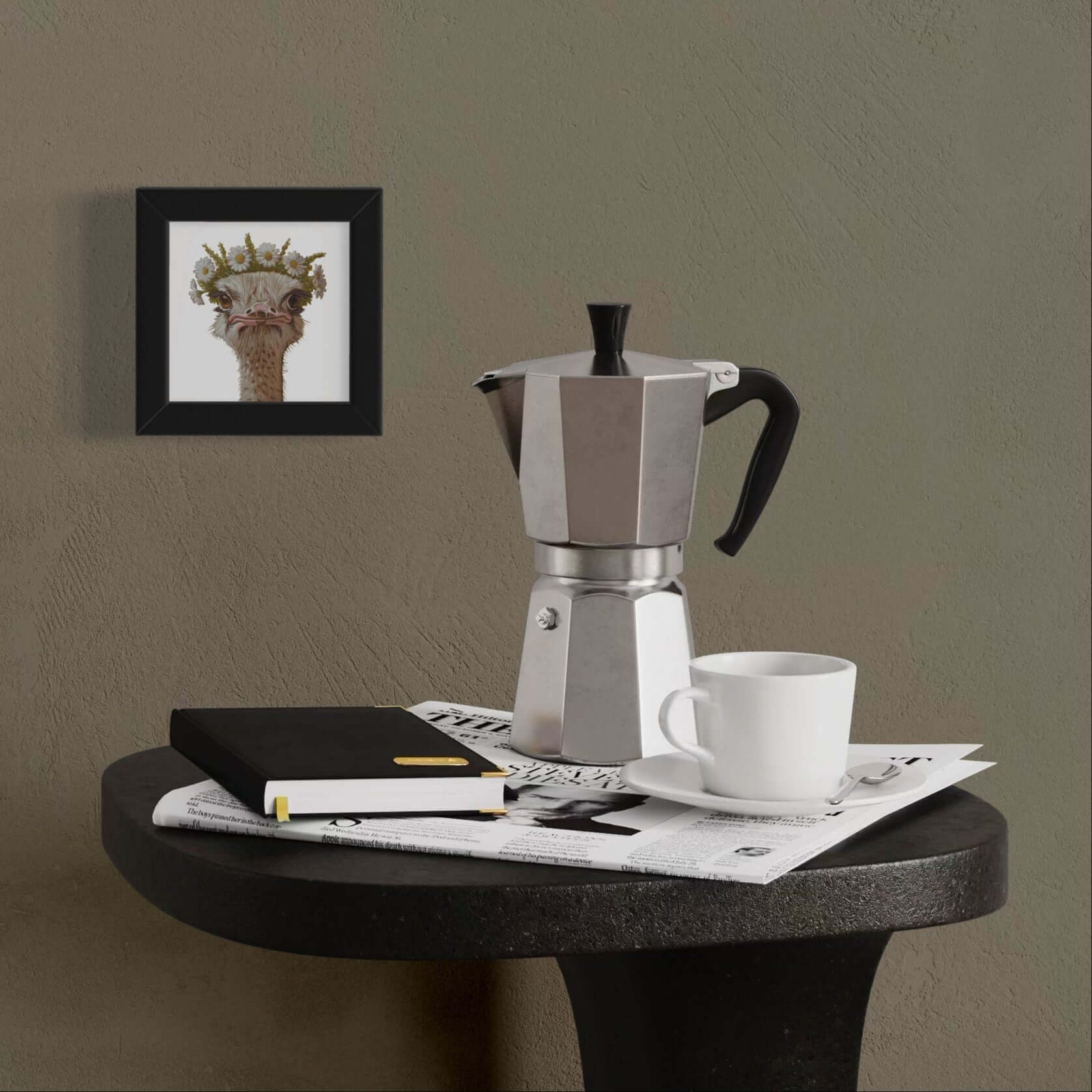 Stylish moka pot, cup, and notebook on a black table with a framed artwork in a modern setting.