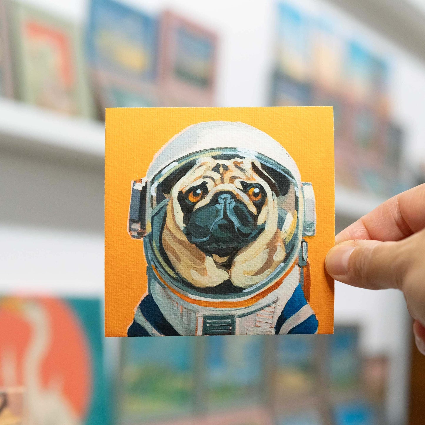 Hand hält Fine Art Print von Mops im Astronautenanzug auf Hahnemühle-Büttenpapier, 10 x 10 cm, gerahmt