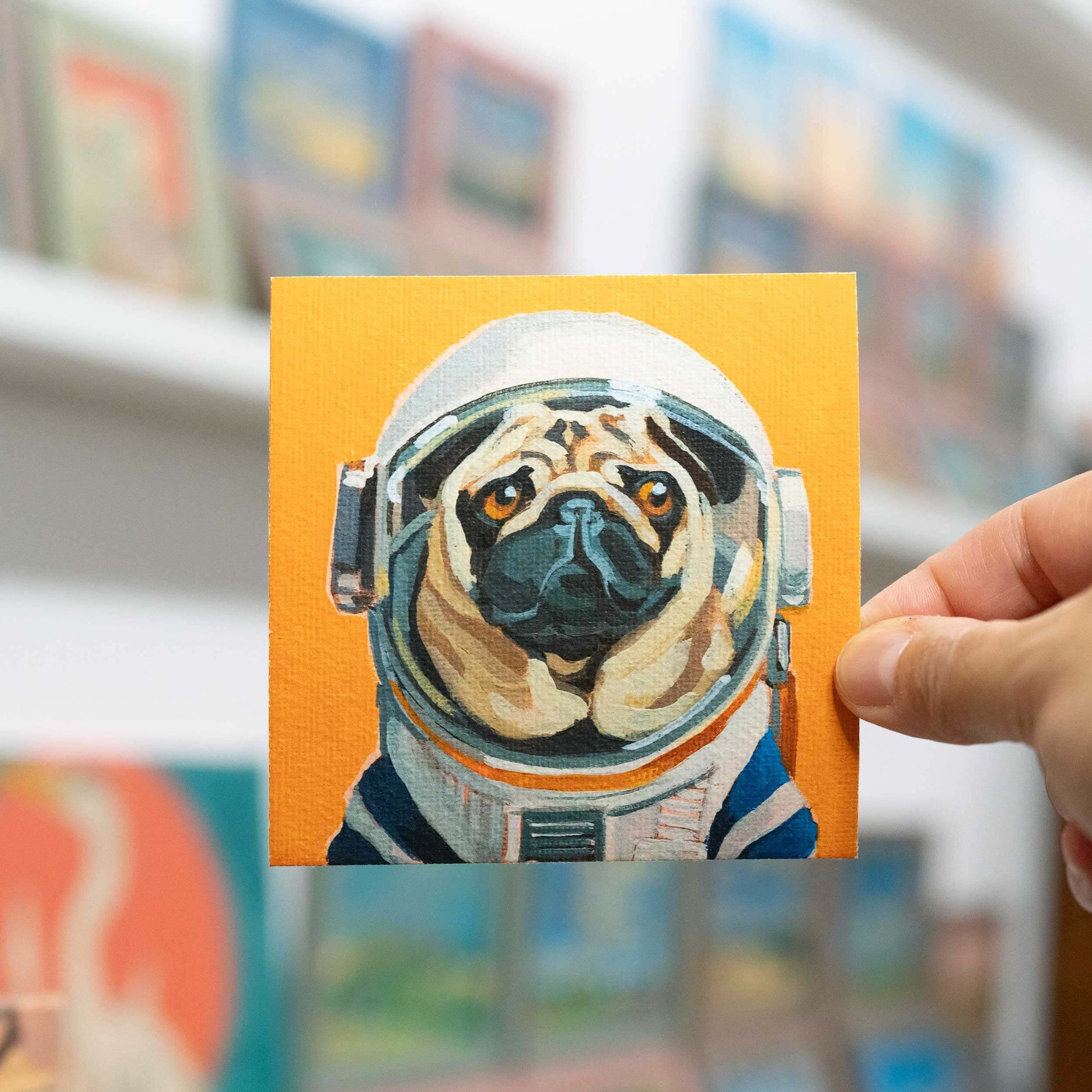 Hand hält Fine Art Print von Mops im Astronautenanzug auf Hahnemühle-Büttenpapier, 10 x 10 cm, gerahmt